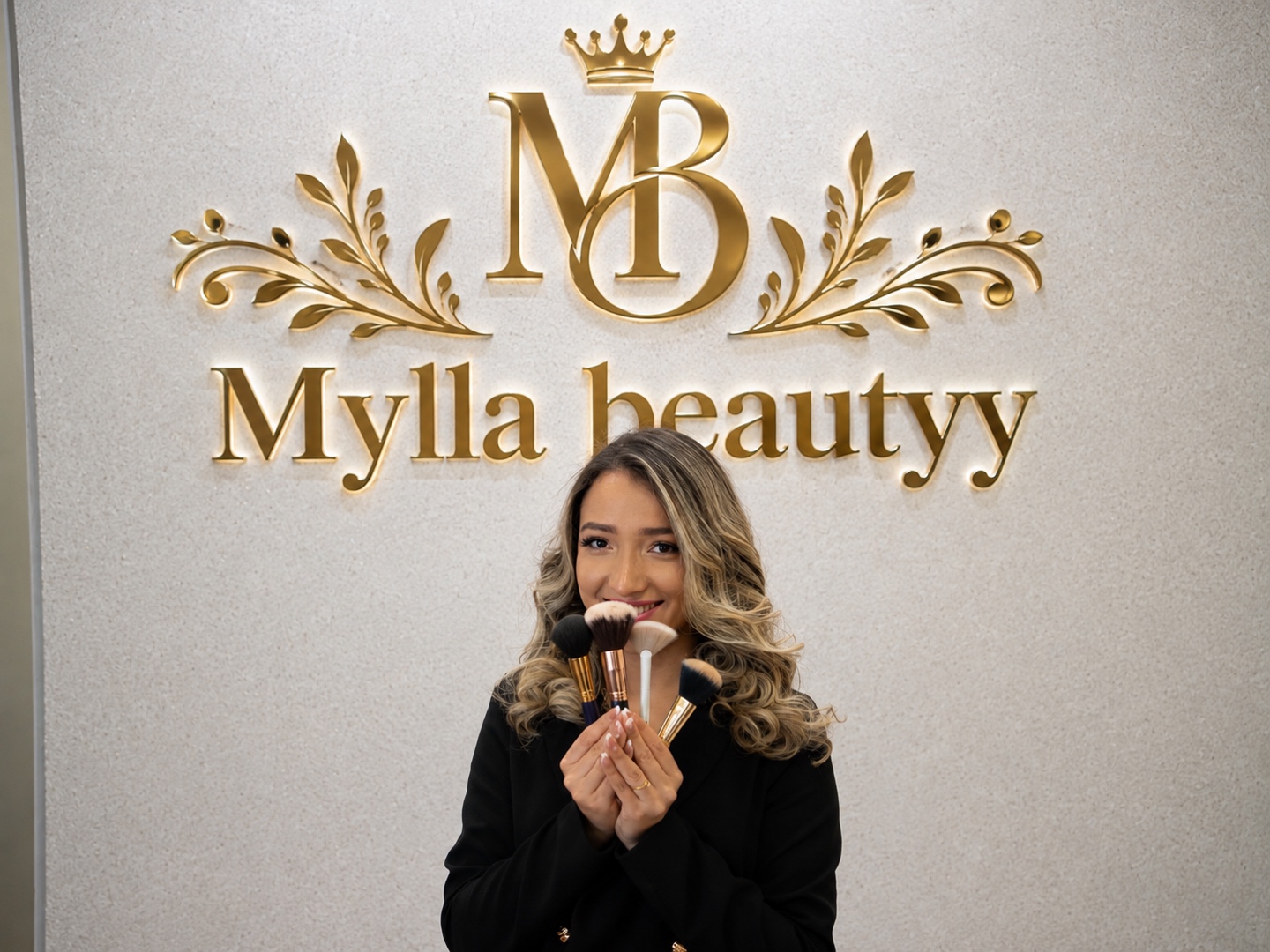 Mylla in front of the Mylla Beautyy logo wall